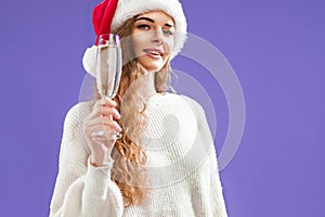 Portrait of happy girl wears in santa hat with glass of champagne on violet background