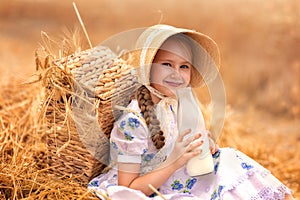 A portrait of a happy girl in a wheat field at sunset. A child holds a glass jar with milk against the background of rye