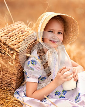 A portrait of a happy girl in a wheat field at sunset. A child holds a glass jar with milk against the background of rye