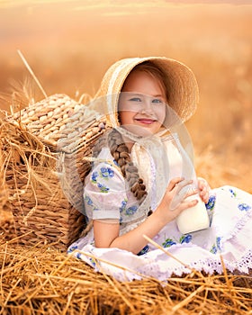 A portrait of a happy girl in a wheat field at sunset. A child holds a glass jar with milk against the background of rye