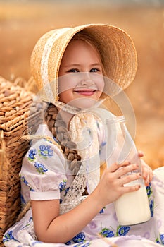 A portrait of a happy girl in a wheat field at sunset. A child holds a glass jar with milk against the background of rye