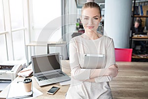 Portrait of happy, good-looking and confident woman sitting t the adge of the table and looking to the camera. She is photo