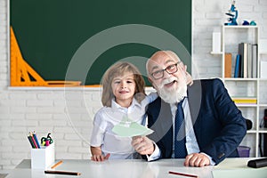 Portrait of happy grandfather and grandson hug, schoolboy pupil embrace teacher in classroom at school. Education in