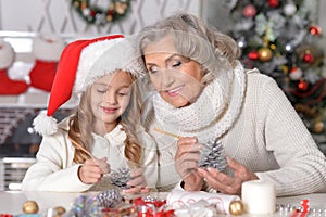 Portrait of happy grandmother and her little granddaughter preparing for Christmas together at home