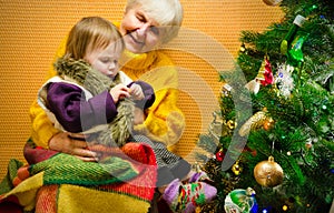 Portrait of happy grandmother hugging her granddaughter over Christmas presents and decorated New Year tree, merry
