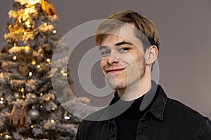 Portrait of a happy guy 20-25 years old on the background of a decorated Christmas tree