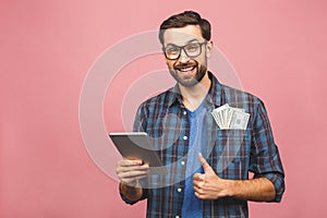 Portrait of happy handsome bearded young hipster man in checkered shirt standing, holding tablet computer and money. Indoor,