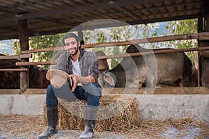 Portrait of happy handsome man cattle farmer owner sitting smiling on the straw stack with looking at camera on organic cow farm