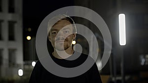 Portrait of a happy handsome man winks at camera in a dark street. Media. Male model posing on camera outside the