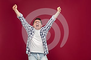 Portrait of happy handsome middle aged man in casual checkered shirt, eyeglasses standing holding hands up, screaming and