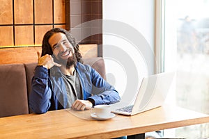 Portrait of happy handsome young adult man freelancer in casual style sitting in cafe with laptop, showing to make call him later