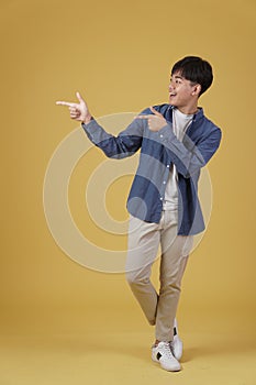 Portrait of happy handsome young asian man dressed casually pointing fingers at copyspace isolated on yellow background