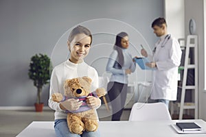 Portrait of a happy healthy little girl hugging a soft toy bear in a clinic in a hospital ward.