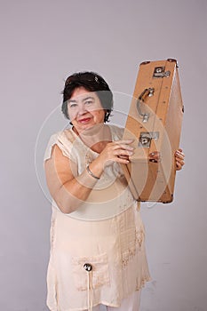 portrait of a happy healthy middle aged woman, with a vintage suitcase on her shoulder, looking at the camera and posing