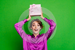 Portrait of happy holiday celebrating young girlfriend raised hands up demonstrate gift box with bun isolated on green