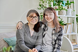 Portrait of happy hugging mother and teenage daughter sitting together on couch