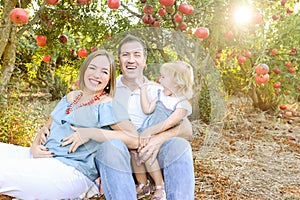 Portrait of happy husbent and pregnant wife with cute baby girl daughter having rest and fun in the pomegrate fruit garden. Family