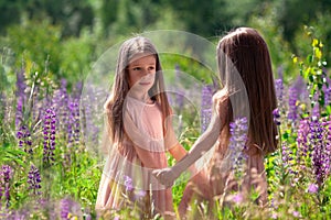 Portrait of happy identical twin sisters with long hair dancing together in beautiful dresses at sunny nature in grass and flowers