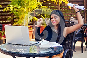 Portrait of a happy Indian business woman working on laptop at summer cafe.remote work freelance serfing