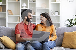Portrait Of Happy Indian Couple With Laptop Relaxing On Couch At Home
