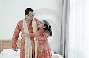 Portrait of happy Indian family standing and hugging in bedroom at home. Smart young father with little cute daughter