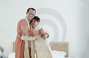 Portrait of happy Indian family standing and hugging in bedroom at home. Smart young father with little handsome son