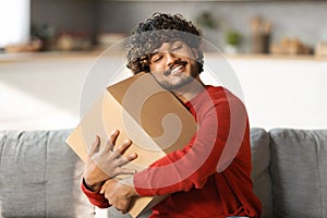 Portrait Of Happy Indian Man Embracing Cardboard Box With Delivery At Home