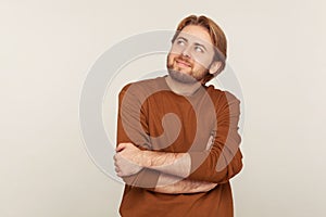 Portrait of happy inspired man with beard wearing sweatshirt looking up with pensive expression