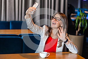 Portrait of happy joyful beautiful stylish brunette young woman in glasses sitting on video call or doing selfie with toothy smile