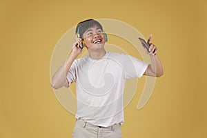 Portrait of happy joyful cheerful young asian man wearing headphones listening to music on smartphone and dancing isolated on