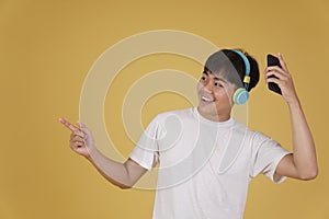 Portrait of happy joyful cheerful young asian man wearing headphones listening to music on smartphone and dancing isolated on