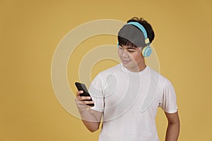 Portrait of happy joyful cheerful young asian man wearing headphones listening to music on smartphone and dancing isolated on