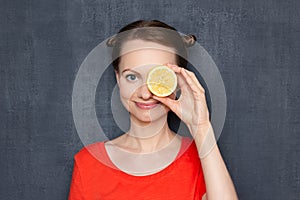 Portrait of happy joyful girl covering eye with half of lemon