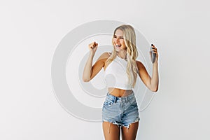 Portrait of a happy joyful girl holding mobile phone and celebrating a win over white background