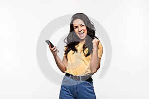 Portrait of a happy joyful woman holding mobile phone and celebrating a win isolated over white background