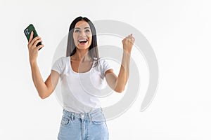 Portrait of a happy joyful woman holding mobile phone and celebrating a win isolated over white background