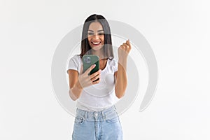 Portrait of a happy joyful woman holding mobile phone and celebrating a win isolated over white background