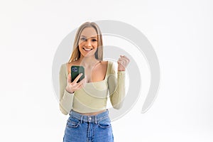 Portrait of a happy joyful woman holding mobile phone and celebrating a win isolated over white background