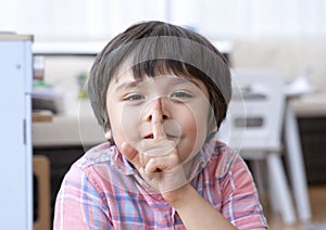 Portrait happy kid boy sitting in play room showing his finger on lips symbol of hush gesture of asking to be quiet, Active chilcd