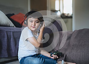 Portrait of happy kid holding video game or game console. Mixed race Child playing game online at home, Young boy siting floor