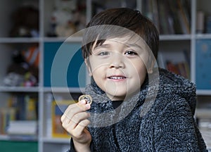 Portrait of Happy kid wearing fulffy pyjamas holding two pound coins, Smiling child boy showing money coins for his saving box