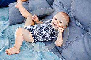 Portrait of happy laughing baby with blue eyes, in blue shirt, sitting on the couch