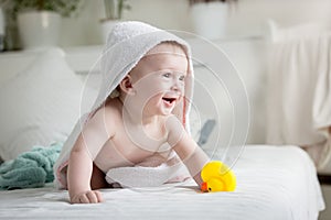 Portrait of happy laughing baby boy covered in white towel paying with yellow rubber duck