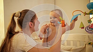 Portrait of happy laughing baby boy with mother playing and having fun in child bed at night