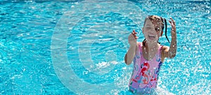 Portrait of happy laughing and playing with water spray 7 years old girl in swimming pool on sunny day