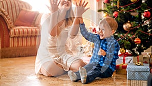 Portrait of happy laughing toddler boy throwing colorful confetti with mother on Christmas morning