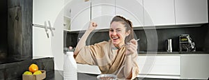 Portrait of happy, laughing young woman eating cereals with milk, triumphing, having breakfast and feeling excited