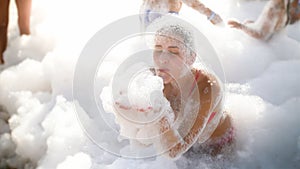 Portrait of happy laughing young woman in red bikini dancing on the sea beach. Girl having fun on sea beach soap foam