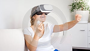 Portrait of happy laughing young woman relaxing on sofa and watching 3D movie in VR headset