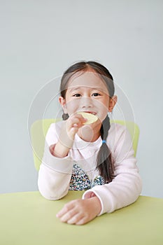 Portrait of happy little Asian child girl eating crispy potato chips on white background. Kid enjoy eating concept
